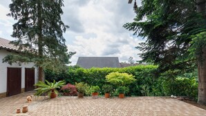 Une cour avec une zone pavée, des plantes en pot et, au fond, un bâtiment doté d’un toit en tuiles.