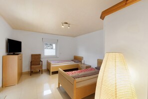 Une chambre à coucher avec deux lits en bois, un téléviseur posé sur une commode, une chaise, une fenêtre et une lampe.