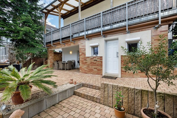 A courtyard with a wooden deck, potted plants, and a brick pathway leading to a door.