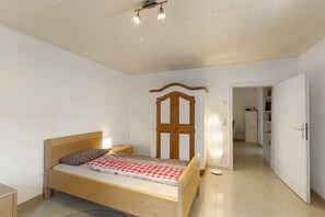 Een slaapkamer met een houten bed, een nachtkastje, een kledingkast en een deur die naar een gang leidt.