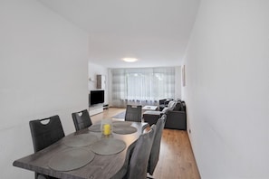 A modern living room with a dining area, a flat-screen TV, and a sofa set.