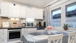 Une cuisine moderne avec des meubles blancs, un four encastré et un coin repas comprenant une table et des chaises.