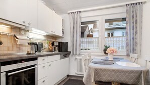 Une cuisine avec des meubles blancs, un four encastré et un coin repas avec une table mise pour deux personnes.