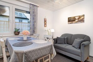 A room with a dining table, a sofa, a window with curtains, and a wall-mounted picture.
