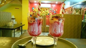 A restaurant interior with a vibrant red and yellow color scheme, a ceiling fan, and a counter with a menu. - Adarsha Palace Hotel (Chuknagar)