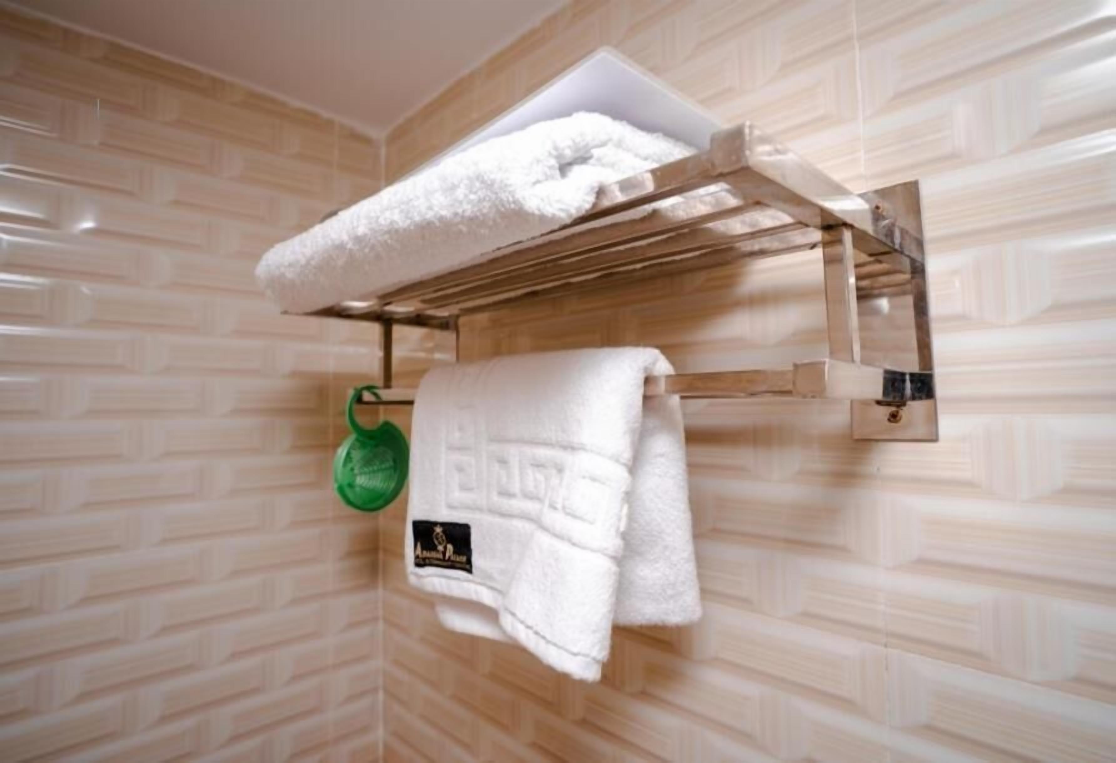 Un baño con un perchero que sostiene dos toallas blancas y una botella verde.