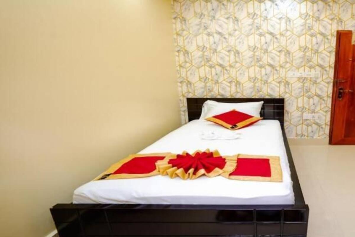 A neatly made bed with a white and red bedspread, a wooden door, and a TV on a wooden stand.