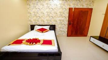 Una cama bien hecha con una colcha blanca y roja, una puerta de madera y un televisor sobre un mueble de madera.