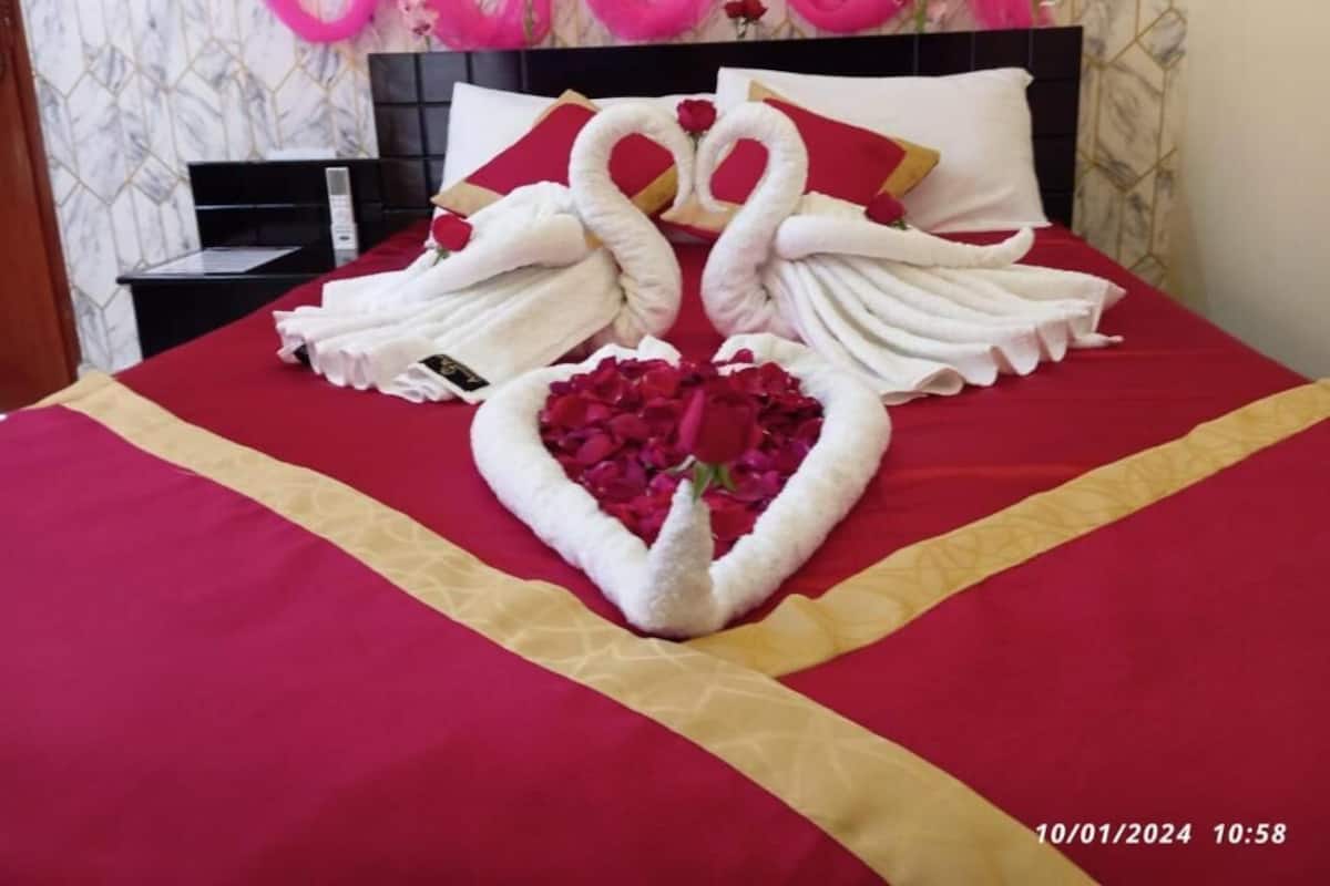A bed with a red and gold bedspread, a heart-shaped arrangement of white towels, and a swan-shaped arrangement of towels.