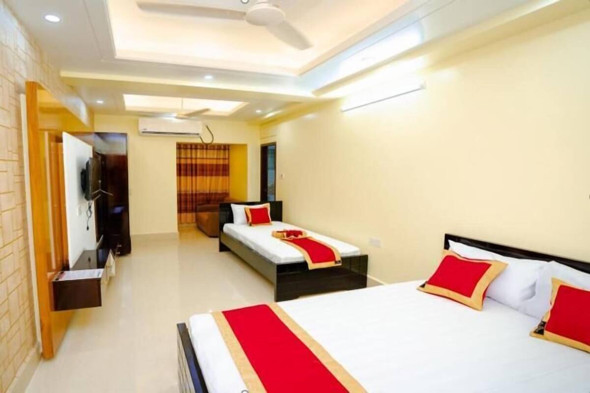 A modern bedroom with a large bed, a smaller bed, a TV, and a ceiling fan.
