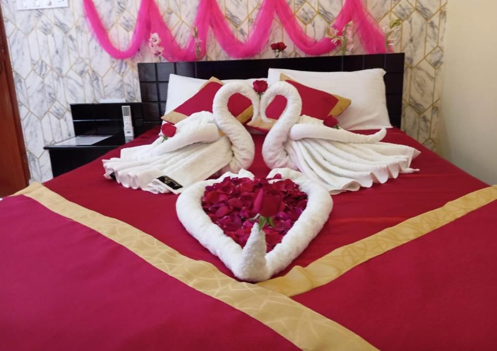 A bed with a red and gold bedspread, a heart-shaped arrangement of white towels, and a swan-shaped arrangement of towels.
