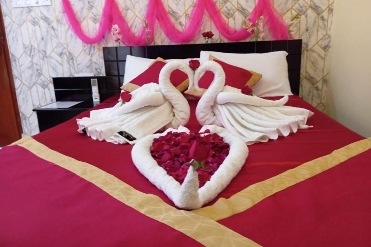 A bed with a red and gold bedspread, a heart-shaped arrangement of white towels, and a swan-shaped arrangement of towels.