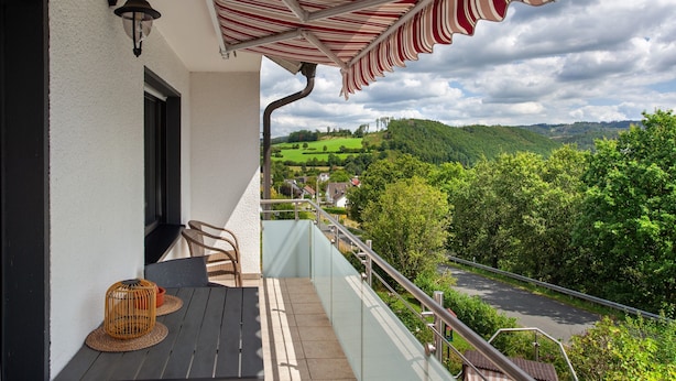 A balcony with a view of a green landscape, a striped awning, and a wicker basket. - Apartment 'Lux' with Private Garden, Balcony and Wi-Fi (Plettenberg)