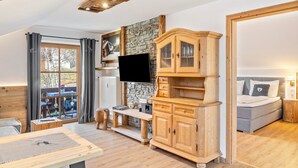 A room with a stone wall, wooden furniture, a flat-screen TV, a bed, and a window with curtains. - Holiday Apartment "Haus Alpenquelle Seeblick" with Mountain View, Balcony & Wi-Fi (Bad Kohlgrub)