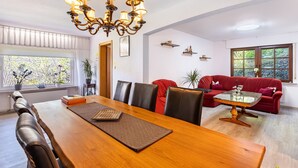 Zona pranzo con tavolo in legno, sedie, un lampadario e un divano rosso.