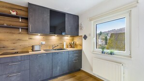 Una cucina moderna con mobili scuri, scaffali in legno, forno integrato e una finestra con vista su un giardino.