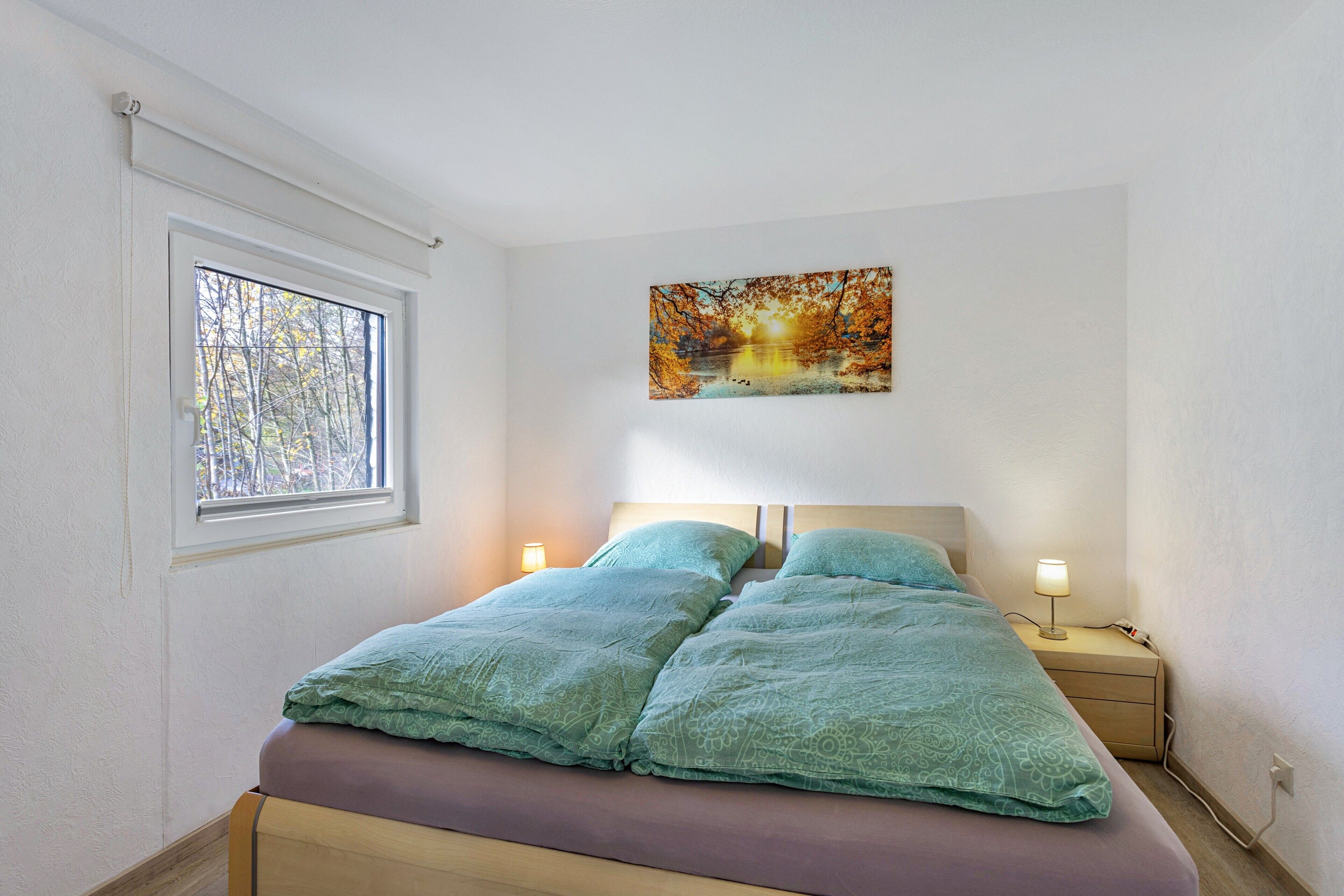 Ein Schlafzimmer mit einem Bett, zwei Nachttischlampen, einem Fenster und einem Wandbild.