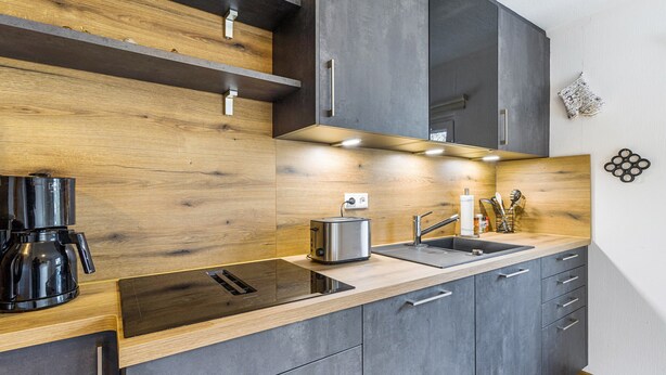 Una cucina moderna con piano di lavoro in legno, elettrodomestici integrati e mobili grigi.
