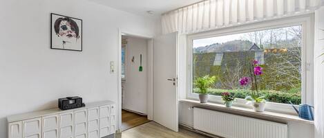 Una habitación con radiador, un armario, una ventana con plantas y una puerta que da a otra estancia.