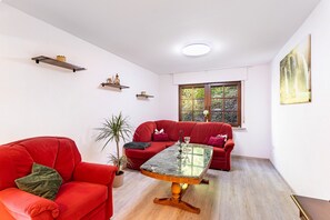 Sala de estar com sofá vermelho, mesa de centro de vidro e janela com vista para o verde.