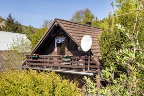 Eine Holzhütte mit geneigtem Dach, einem Balkon mit Sitzgelegenheit und einer Satellitenschüssel.