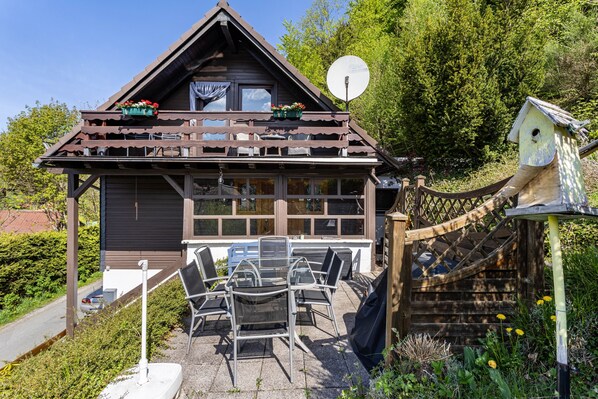 Eine Holzhütte mit Balkon, Sitzgelegenheit im Freien und einem Vogelhäuschen.