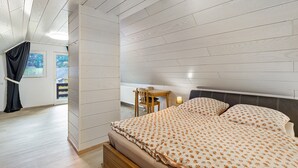 Una camera da letto con soffitto in legno, un letto con biancheria da letto floreale, un comodino e una finestra con tende.