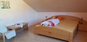 Un dormitorio con cama, mesita de noche, silla y estante en la pared.