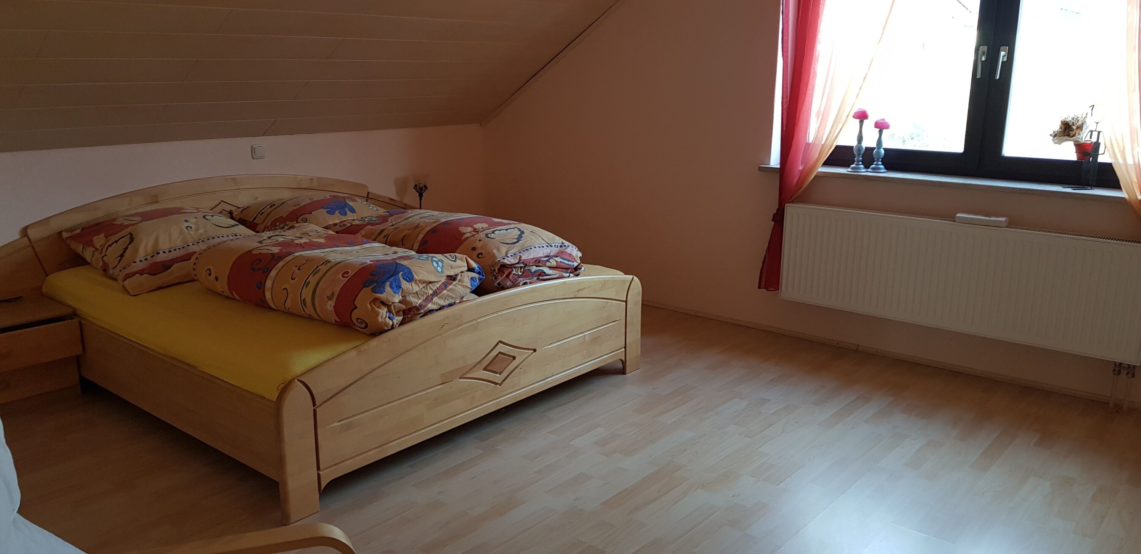 Ein Schlafzimmer mit einem hölzernen Bett, einem Heizkörper und einem Fenster mit Vorhängen.
