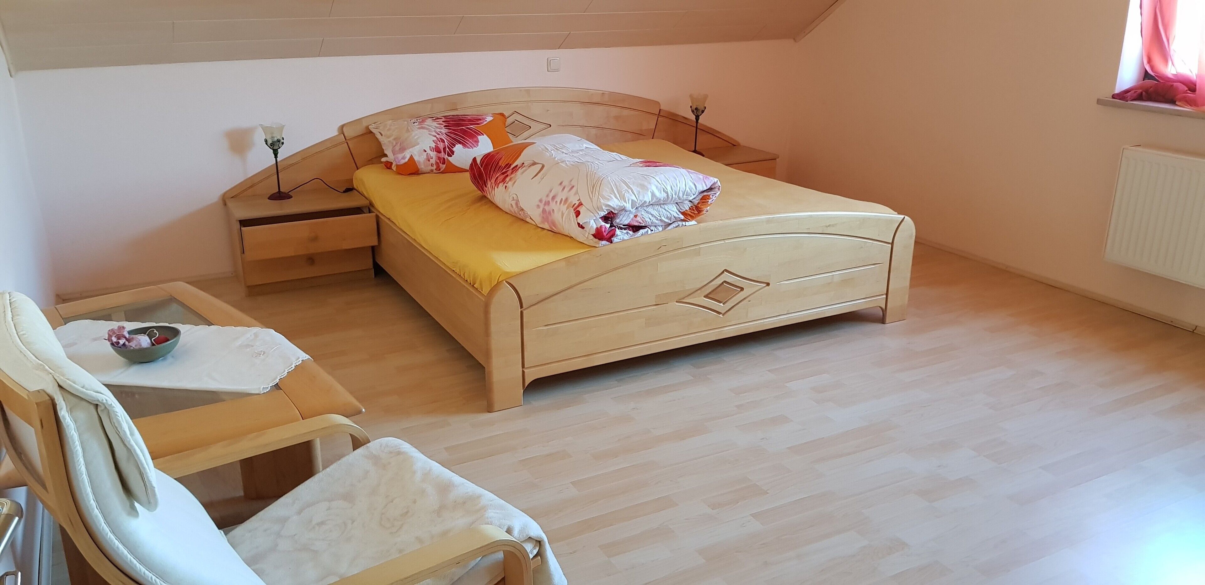 Une chambre à coucher avec un lit en bois, une table de chevet, une chaise et une fenêtre.