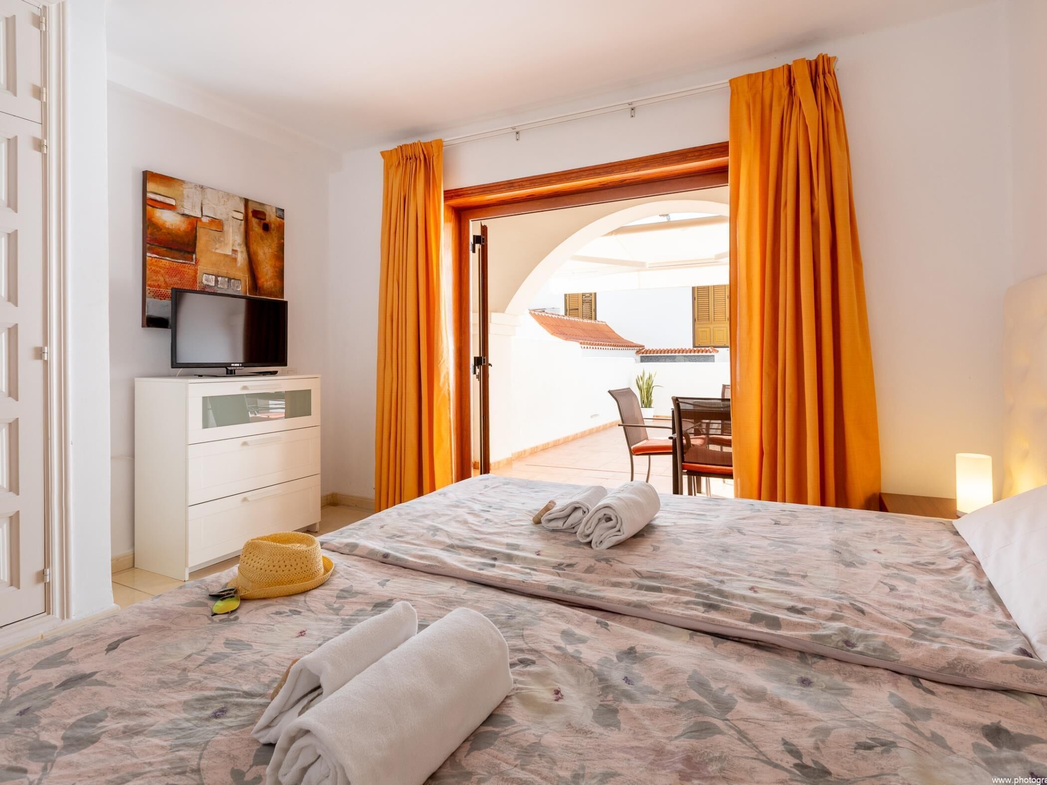 Quarto de hotel com cama, televisão, escrivaninha e vista para a área externa.