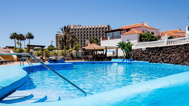 A swimming pool with a clear blue water, a lifeguard stand, and a rock feature. - Paraiso Royal I, Sunny Terrace & Heated Pool (Playa de las Américas)