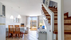 A spacious living area with a dining table, chairs, and a sofa. A staircase leads to an upper level with a balcony. - 395 Lovely Duplex Parque Santiago II (Playa de las Américas)