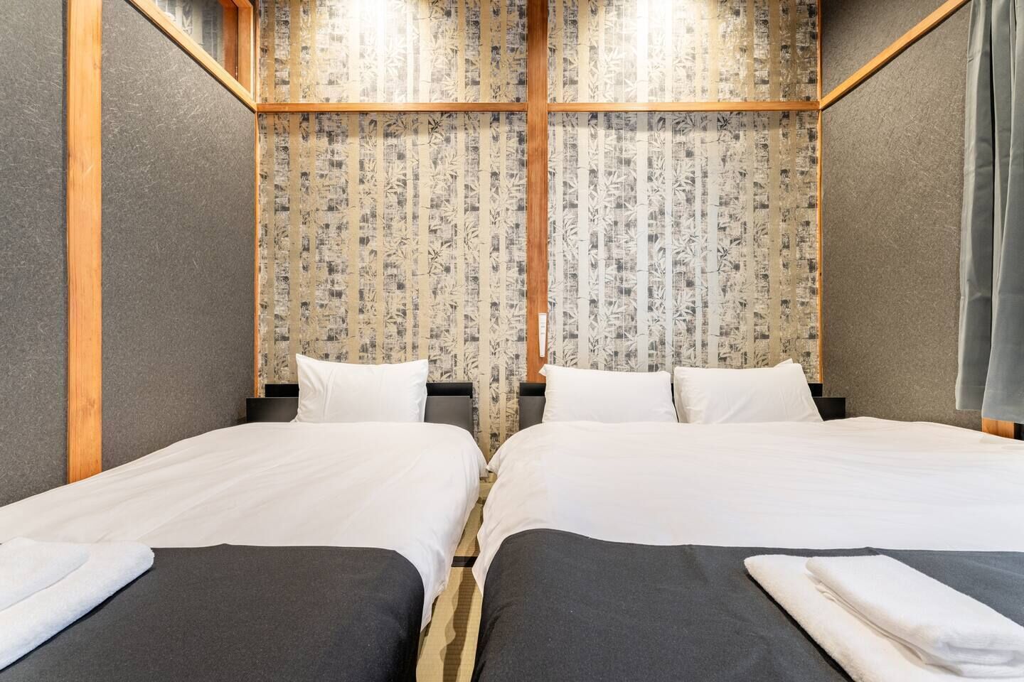 Habitación con dos camas, cada una con cabecero oscuro y ropa de cama blanca. Las paredes tienen un papel tapiz con un diseño vertical.