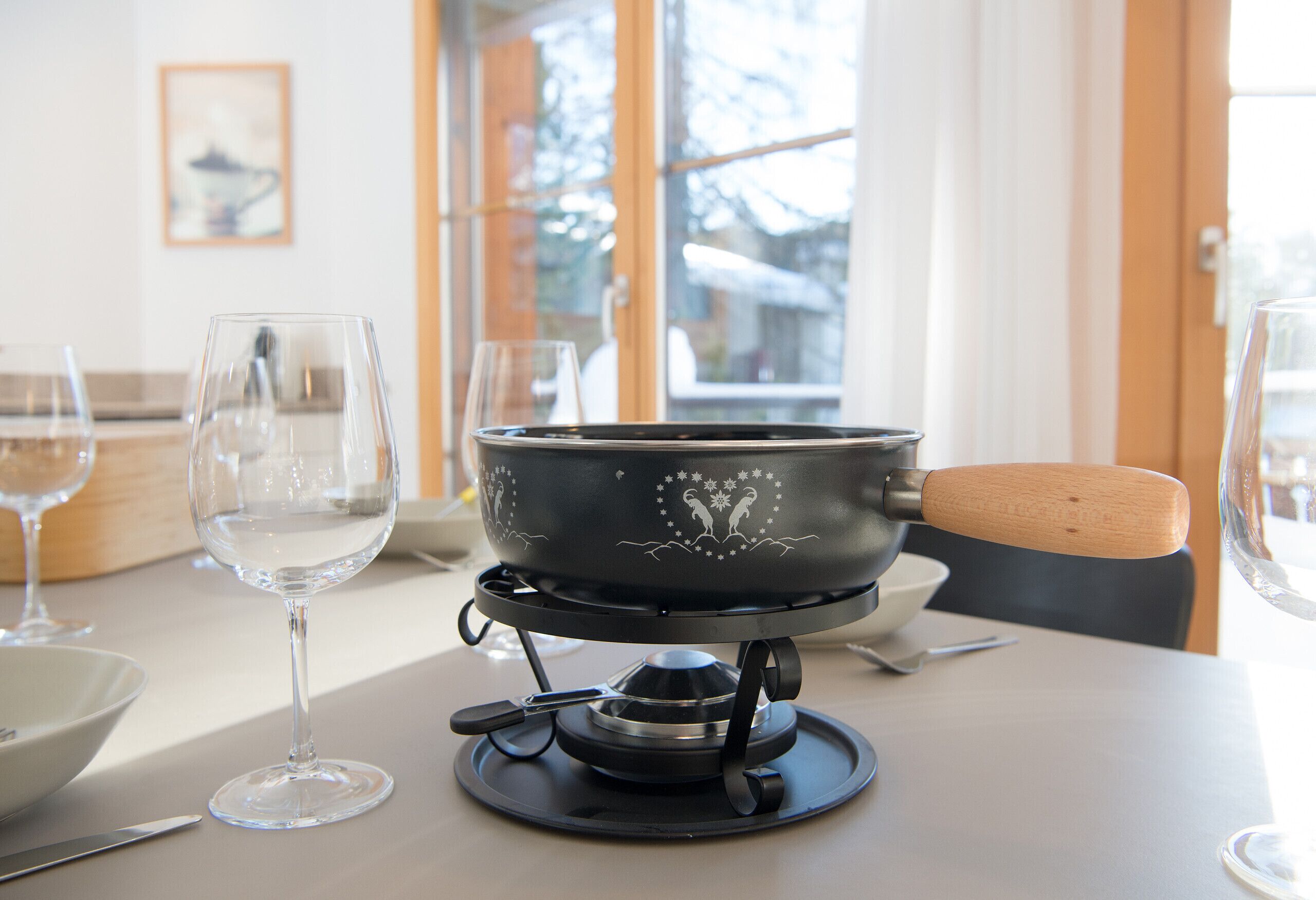 A dining table with a portable stove, wine glasses, and a bowl.