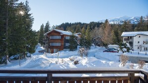 Eine Holzhütte mit schneebedecktem Dach, umgeben von Bäumen und einem Berg im Hintergrund.