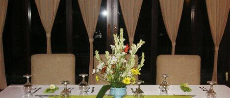 A dining table set for two with a vase of flowers, green napkins, and cutlery.