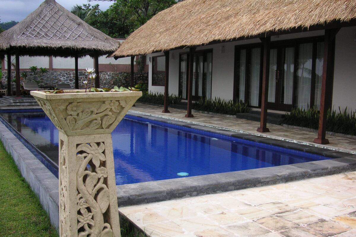 A swimming pool with a stone border, surrounded by a stone pathway and a decorative planter.
