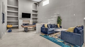 A modern living room with a grey sofa, a coffee table, and a blue rug. There is a TV mounted on the wall and a plant in the corner. - Grand Casa (Las Vegas)