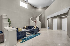 A spacious living area with a curved staircase, a dark grey sofa set, and a blue patterned rug. - Grand Casa (Las Vegas)