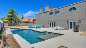 A swimming pool with a stone facade house, outdoor seating, and a clear blue sky. - Grand Casa (Las Vegas)