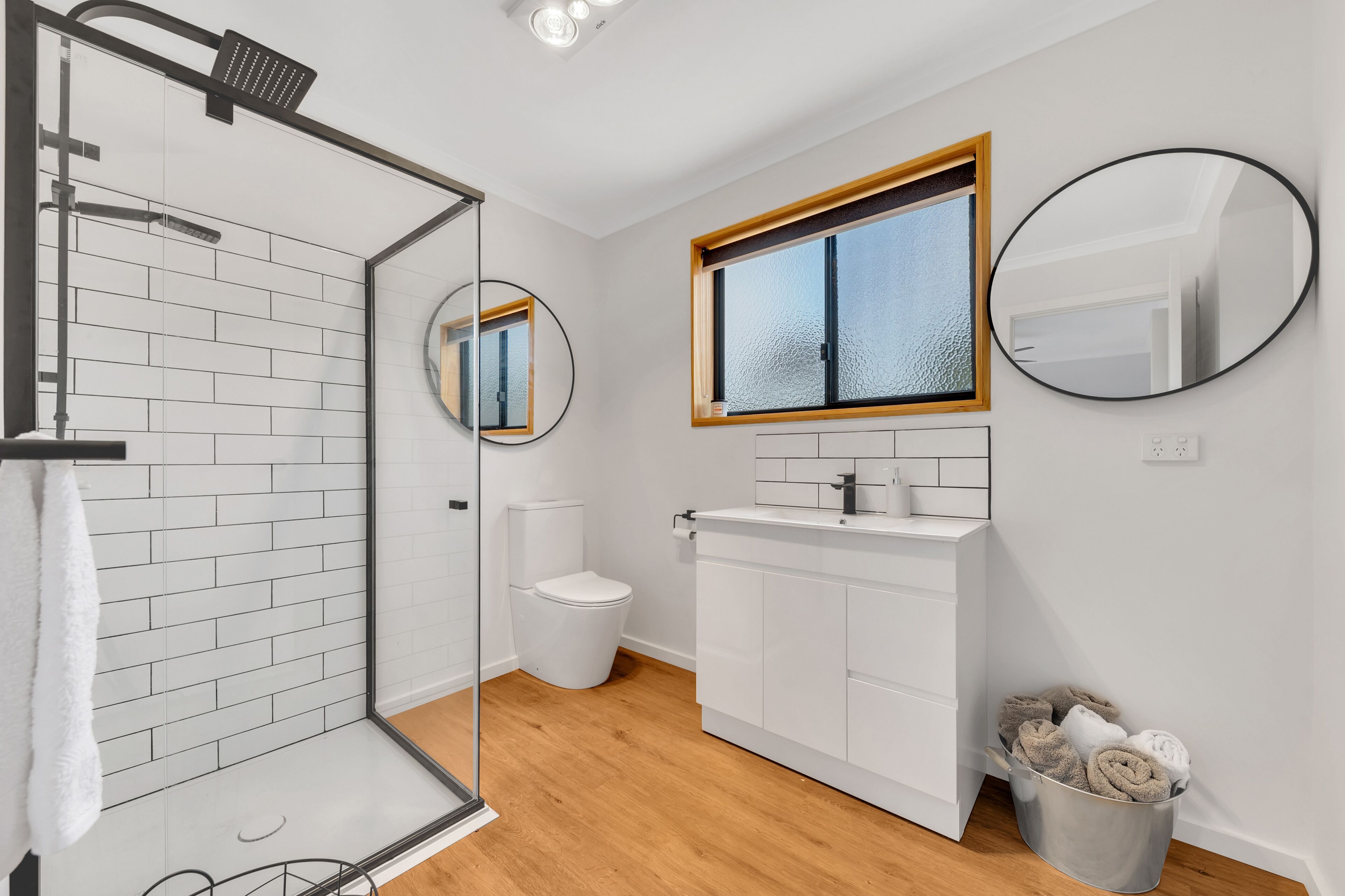 Un baño moderno con cabina de ducha de vidrio, inodoro, lavabo con espejo y ventana.