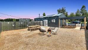A backyard with a gravel patio, a wooden picnic table, and three white wire-framed chairs. - Brand New Family/ Work Cottage
3Bed1.5Bath
1King size with Tv 
2 queen size bed (Bannockburn)