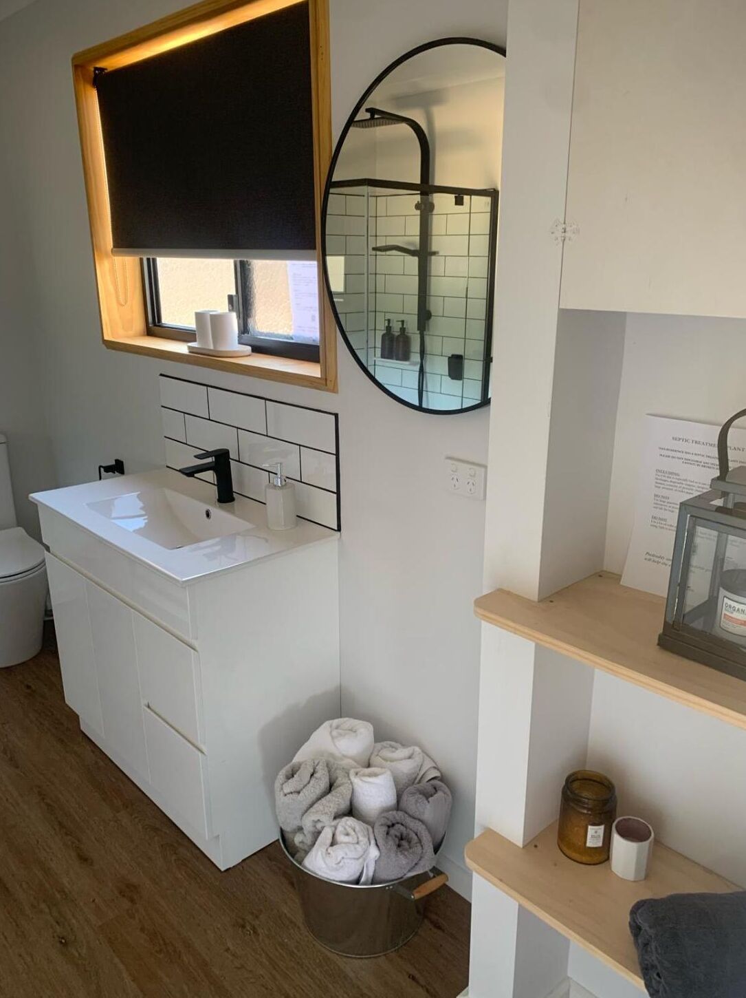 A modern bathroom with a white sink, a mirror, a toilet, and a shelf with toiletries.
