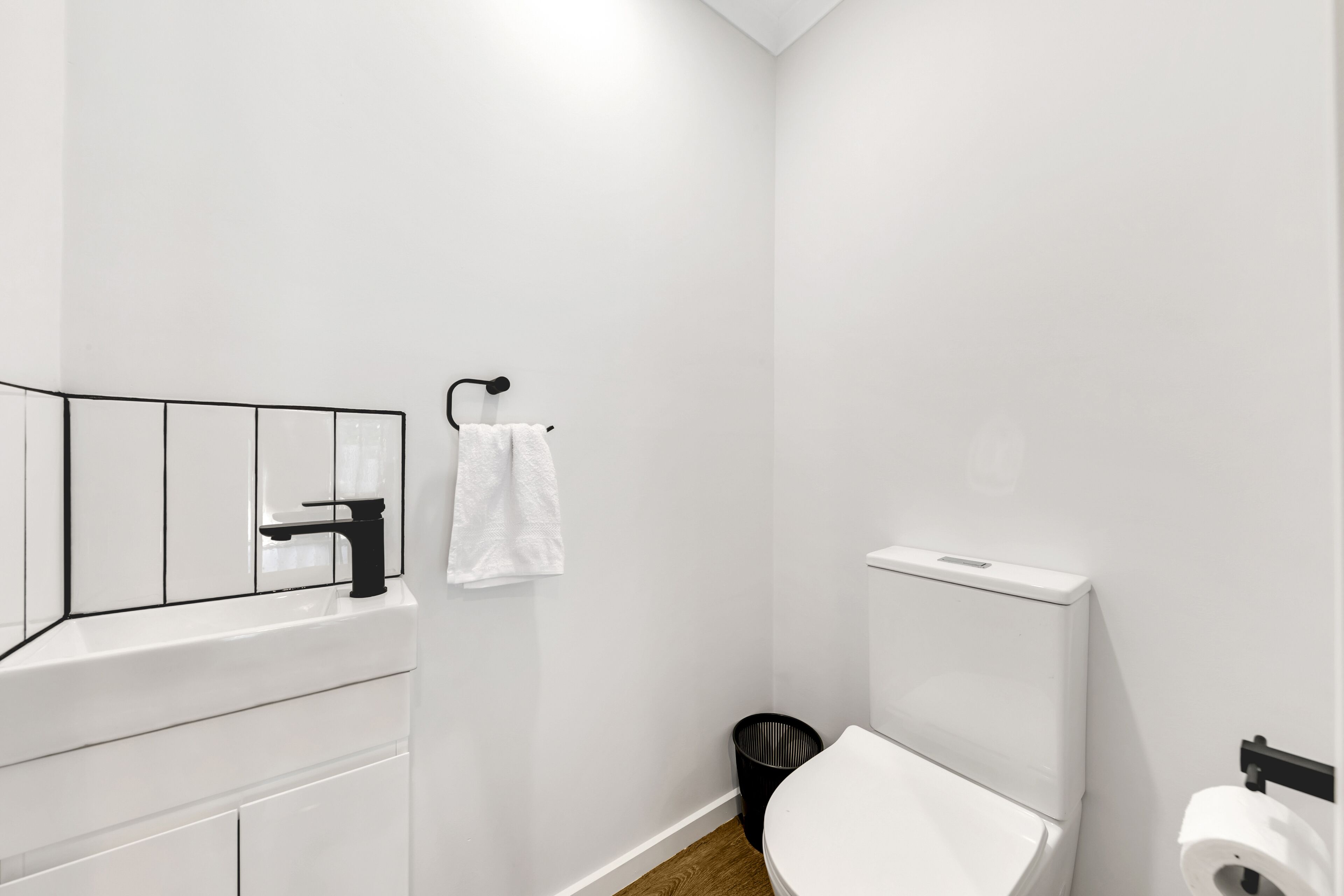 Un bagno con lavandino bianco, rubinetto nero, WC bianco e cestino nero.