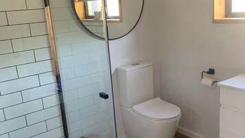 A modern bathroom with a glass shower enclosure, a white toilet, and a round mirror.