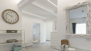 Et moderne, minimalistisk værelse med et rundt vægur, hvide reoler med kurveflet, et glasbord og et unikt hvidt trækunstværk.