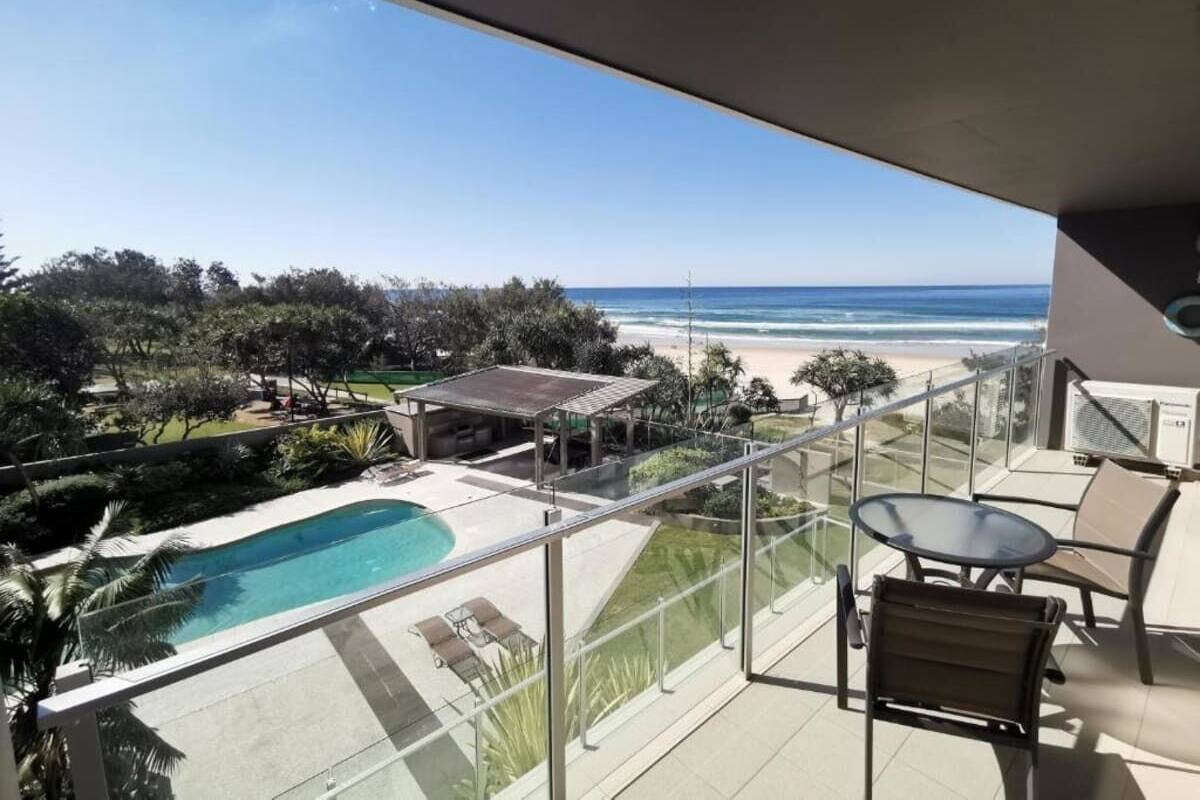A balcony with a pool, outdoor seating, and a view of the beach.
