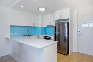 A modern kitchen with white cabinets, a blue backsplash, and a stainless steel refrigerator.
