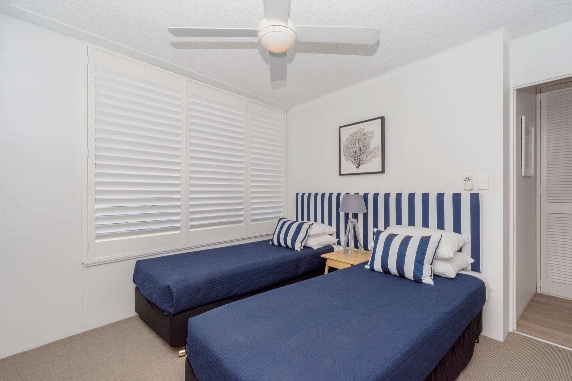 A bedroom with two beds, a ceiling fan, a bedside table with a lamp, and a framed picture on the wall.